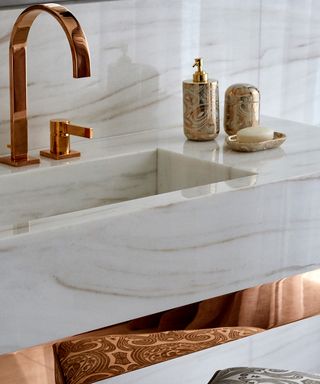 A white marble sink with rose gold faucet, illustrating the metallic glamor bathroom trend 2021.