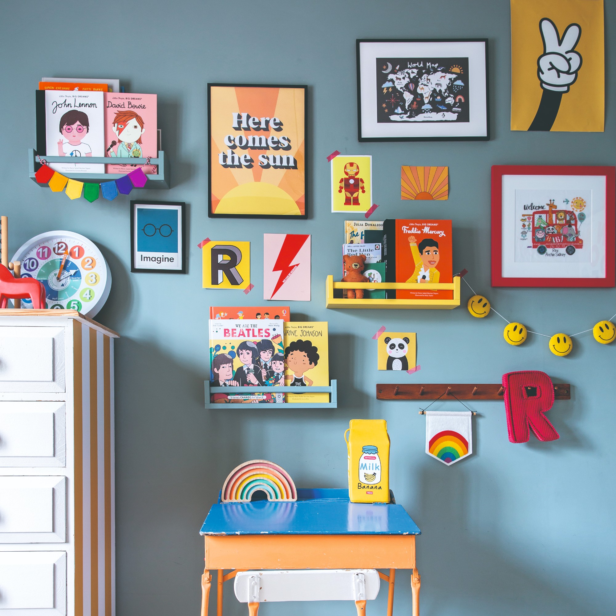 A blue-painted children's room with colourful wall decor and a small desk