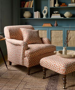 Orange upholstered armchair with footstool in front of blue shelves