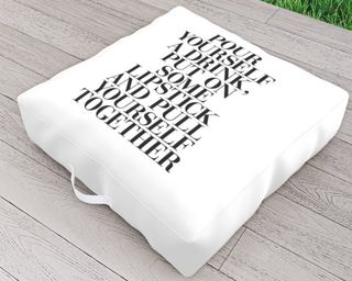 A white outdoor cushion with slogan text 'Pour yourself a drink, put on some lipstick and pull yourself together'