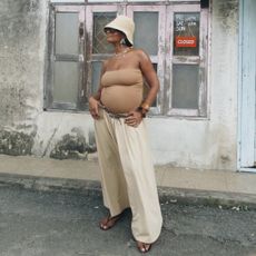 A woman wears a straw hat, tube top, and beige pants with flip-flops.