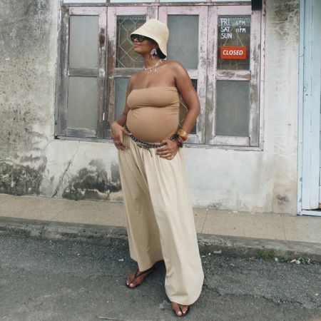 A woman wears a straw hat, tube top, and beige pants with flip-flops.