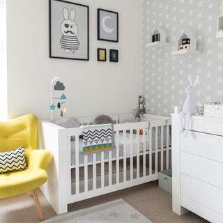 Scandi-style nursery with grey wallpapered feature wall, white cot, and bright yellow armchair