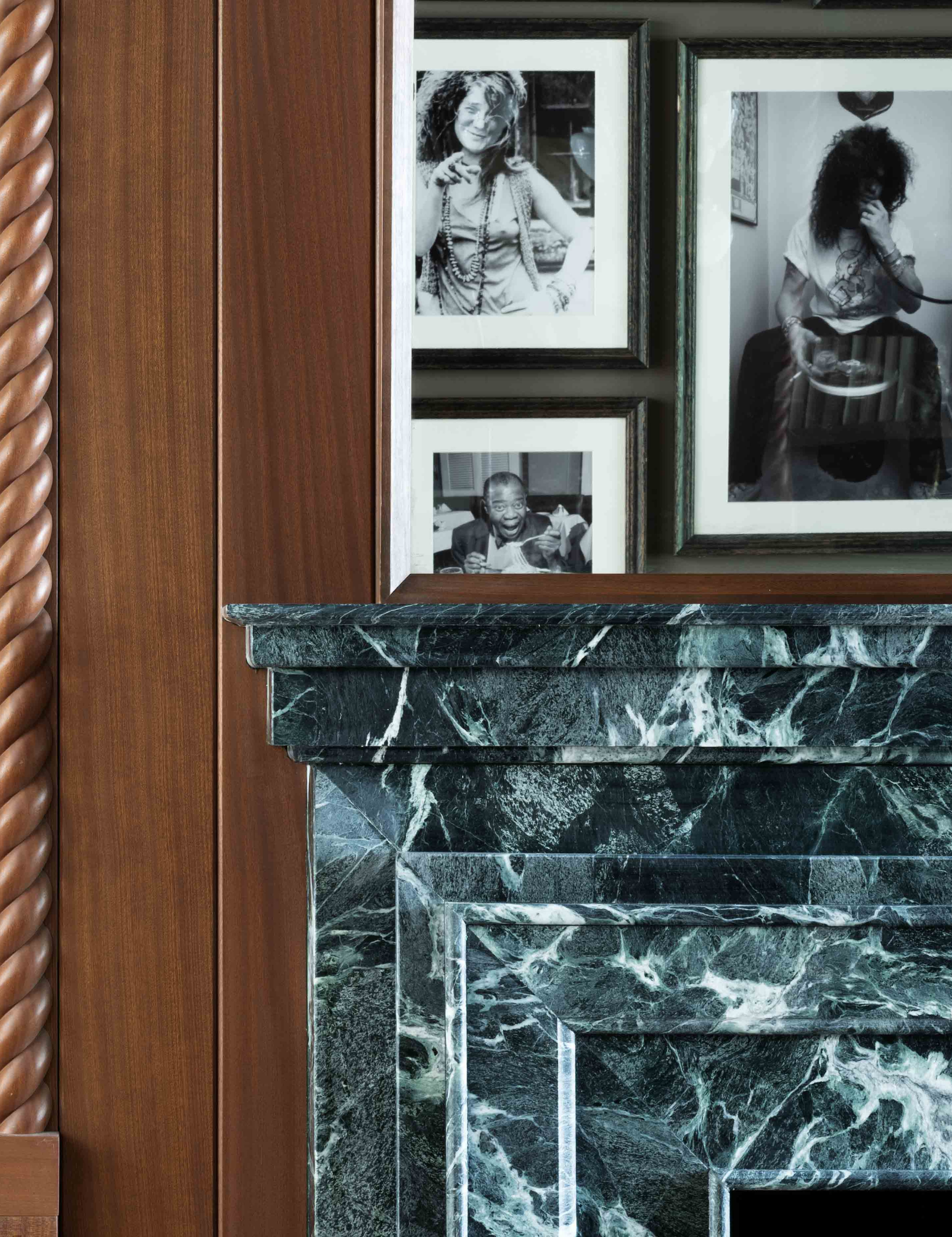 Black-and-white gallery wall seen in the reflection of a mantle mirror against a wood paneled wall overlooking a marble fireplace