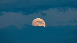 a large full moon partially obscured by blue hued clouds.