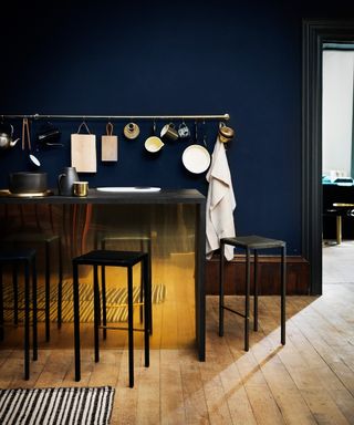 Kitchen color ideas in dark blue with wooden flooring and a brass island with black stools.