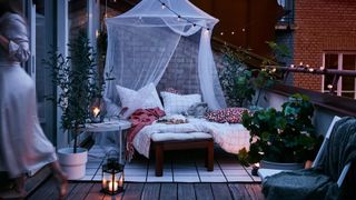 wooden chairs with cushions and a duvet on a balcony with a net canopy covering the chairs