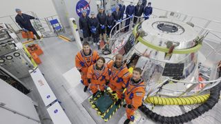 four people in orange flight suits sit inside a drab-looking office room