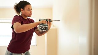 A woman drilling into a wall