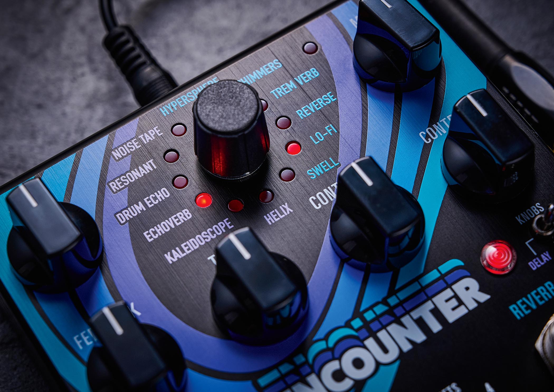 The Source Audio Encounter delay and reverb pedal is photographed here in close-up against an industrial metal background.