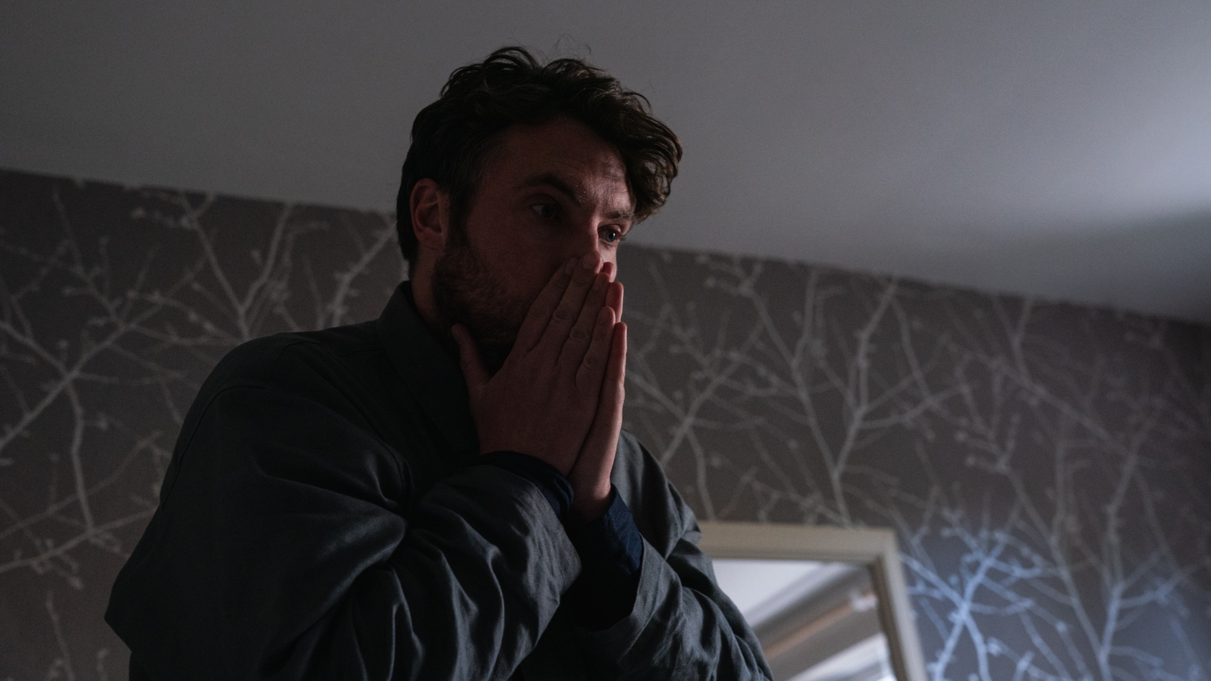 James with his hands to his face in shock as he finds Maria dead on her sofa 