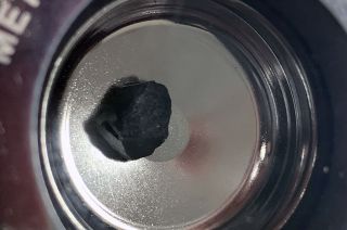 closeup of a small black rock sitting on a silver tray