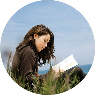 Young girl sitting in a grass field reading a book