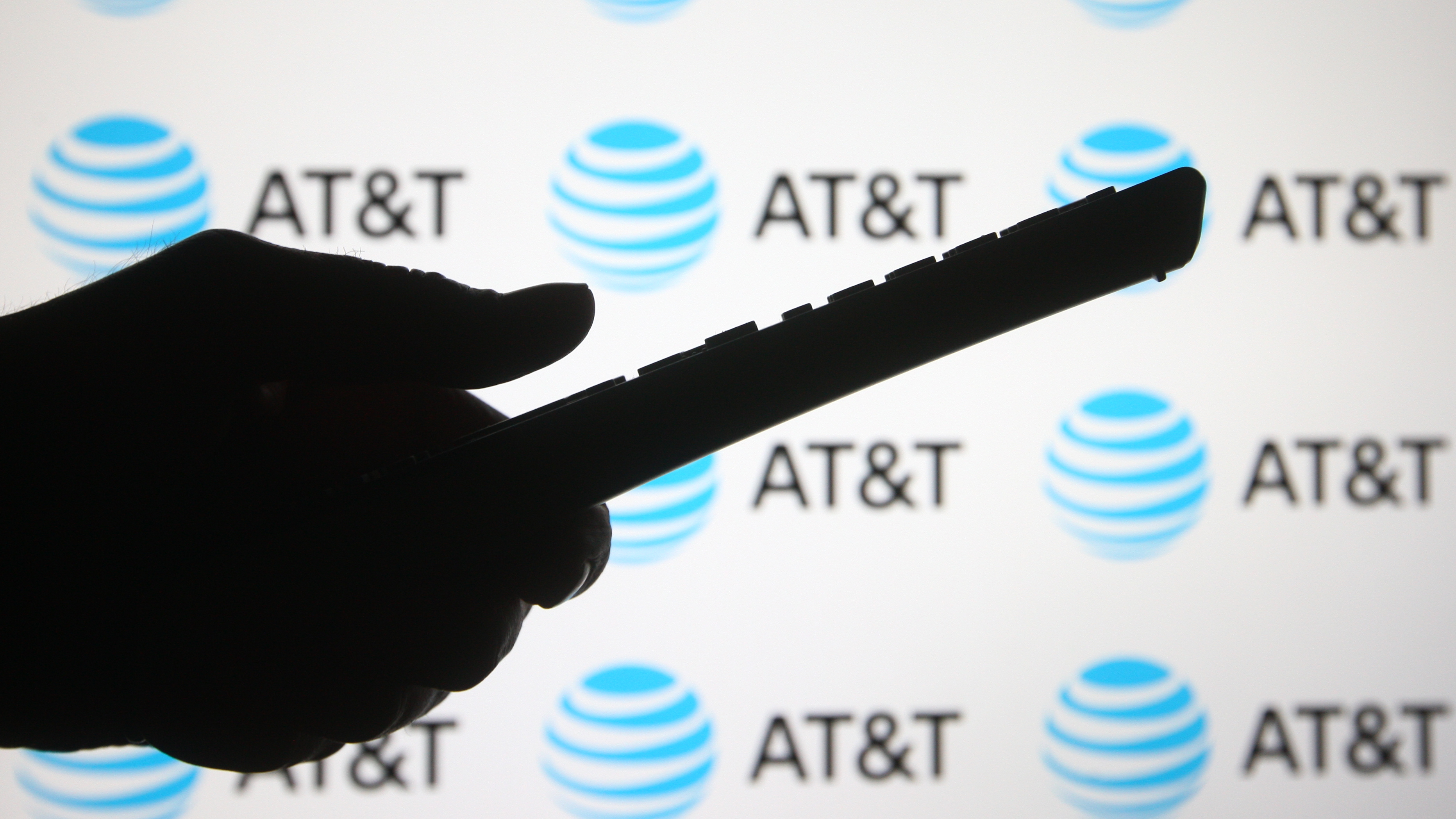 The silhouette of a hand holding a phone in front of the AT&amp;amp;T logo