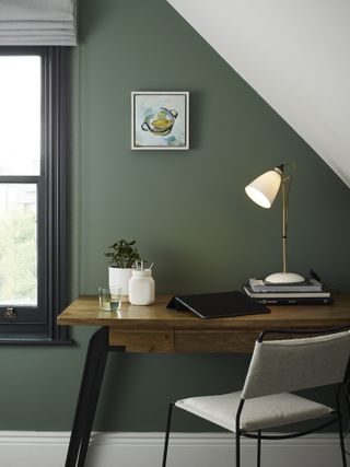 green bedroom home office with wood and metal desk, metal chair, desk lamp, window frame painted black, blind