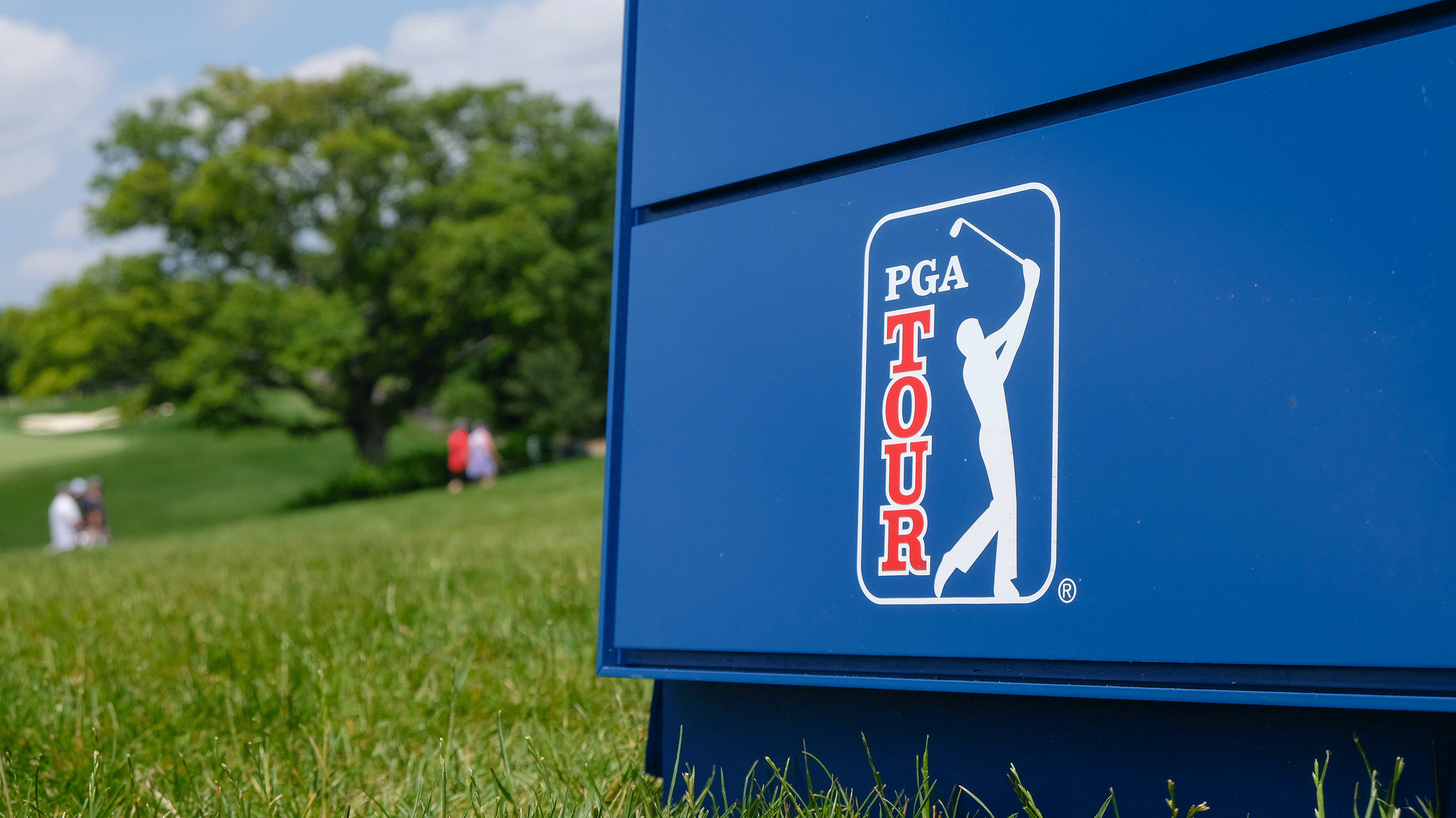 A PGA Tour sign on a blue background with a golf course in the background to the left