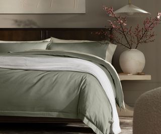 Green and white blankets, sheets, and pillows on a bed against a light brown wall.