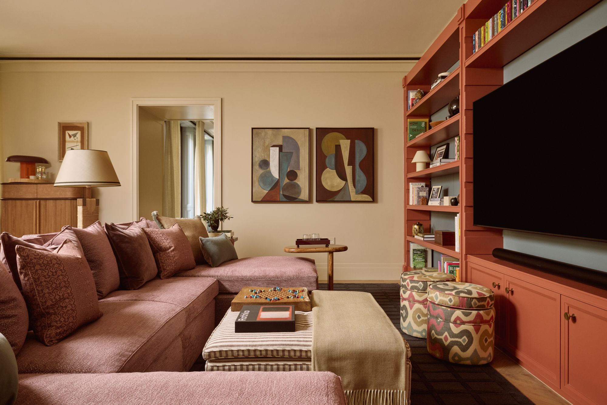 a media room with a large clay red couch, an ottoman, a large TV, and a built-in bookshelf holding books and decorative objects