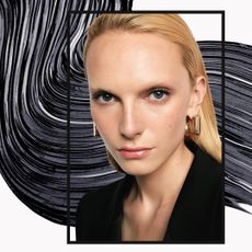A picture of a blonde woman with fair skin enclosed in a black border. She is in front of an abstract mascara swatch. Beside her is a silver tube of YSL mascara. 