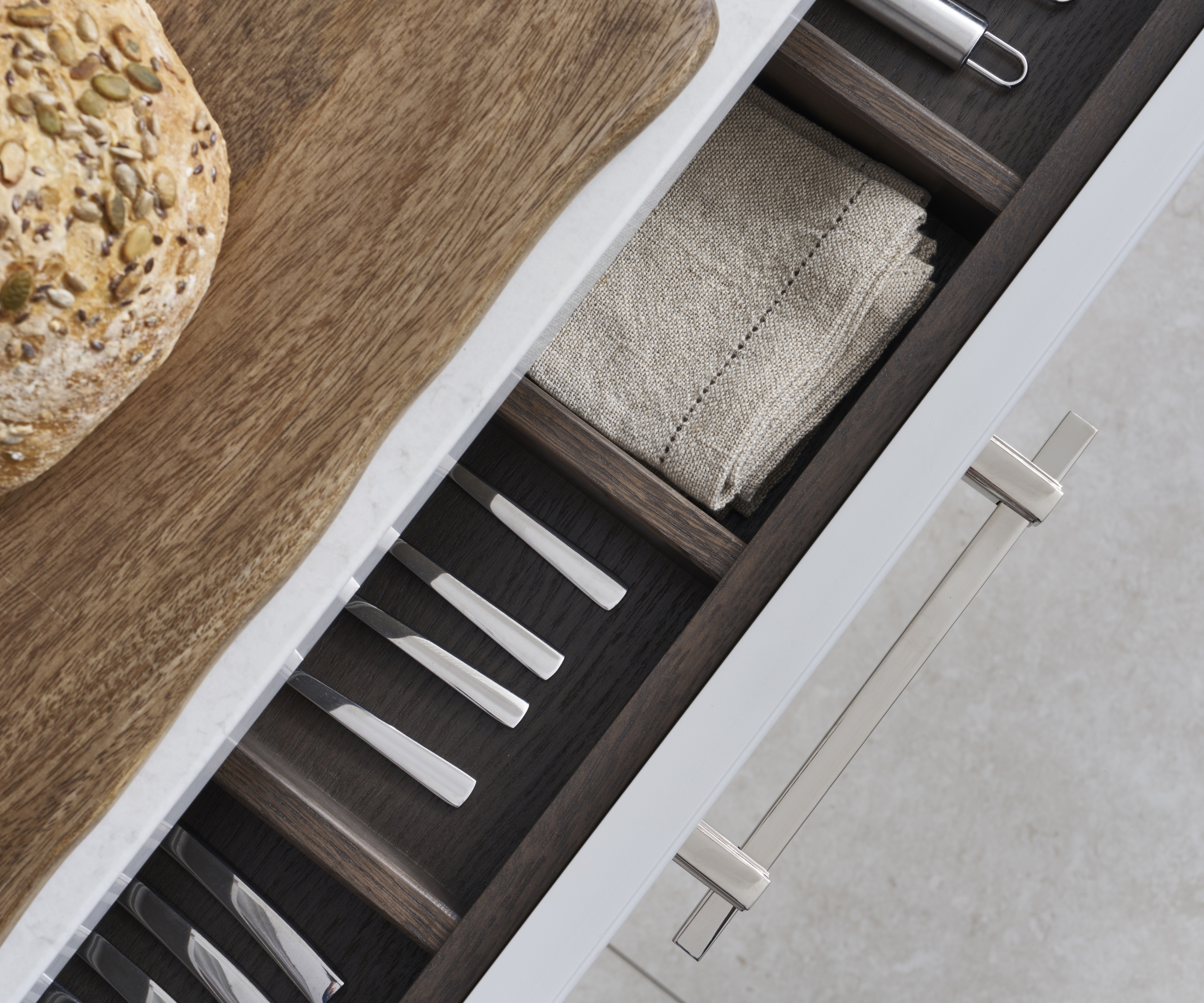 close up of open kitchen drawer with matt chrome handle and dark wooden insert inside drawer