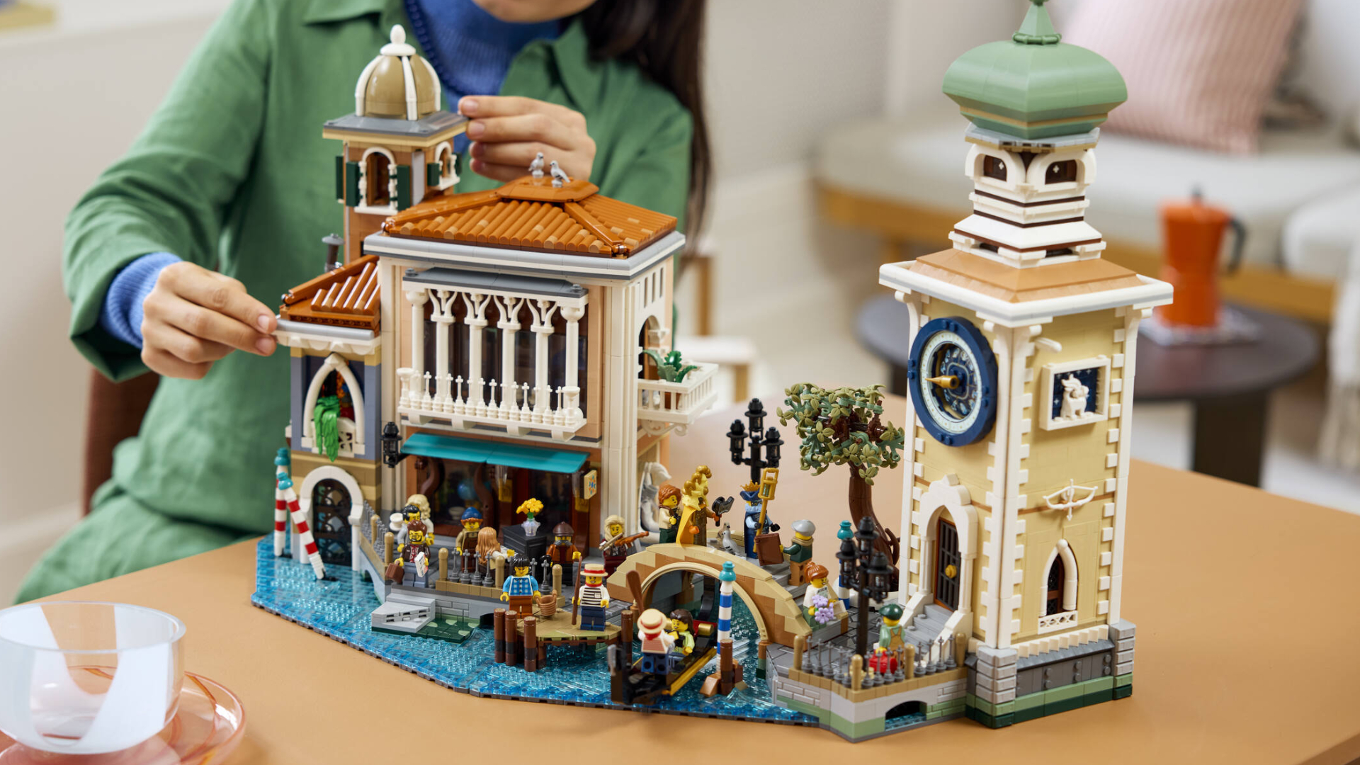 A woman places pieces onto the finished Lego Venetian Neighborhood, which sits on a wooden table