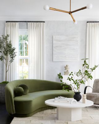 White living room with cream rug, white coffee table and green velvet curved sofa