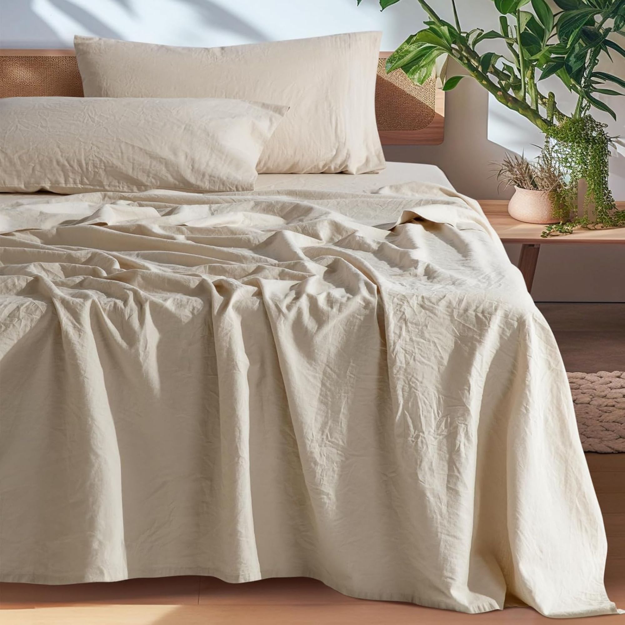 SONORO KATE 100% French Pure Linen Sheets on a bed against a white wall; to the left, a houseplant on a nightstand. 