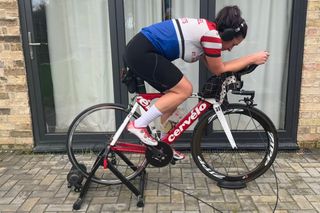 Caroline Harding riding her time trial bike on a turbo trainer outside in front of glass patio doors