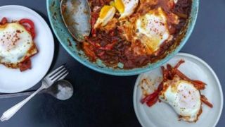 overhead shot of a big platter of shakshuka, flanked by two plates with servings of shakshuka