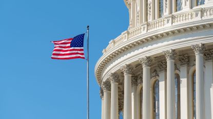 An American flag flying outside the US Capitol building against a blue sky