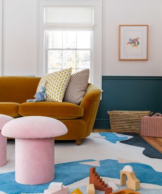 playroom with dark blue lower wall, gold velvet sofa, pink stools, blue, white and pink patterned rug