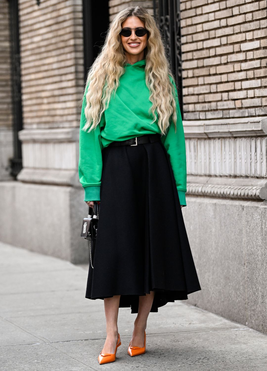 Emili Sindlev is seen wearing a green hoodie, black skirt, black belt and orange shoes with a NY Yankees black bag outside the Coach show during New York Fashion Week F/W 2023 on February 13, 2023 in New York City