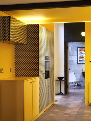 Jason Mclean house in Camberwell. Kitchen with yellow and patterned cupboards, oven and brown floor tiles.