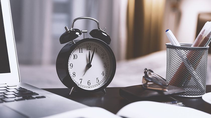 An image of an alarm clock on a desk next to a laptop