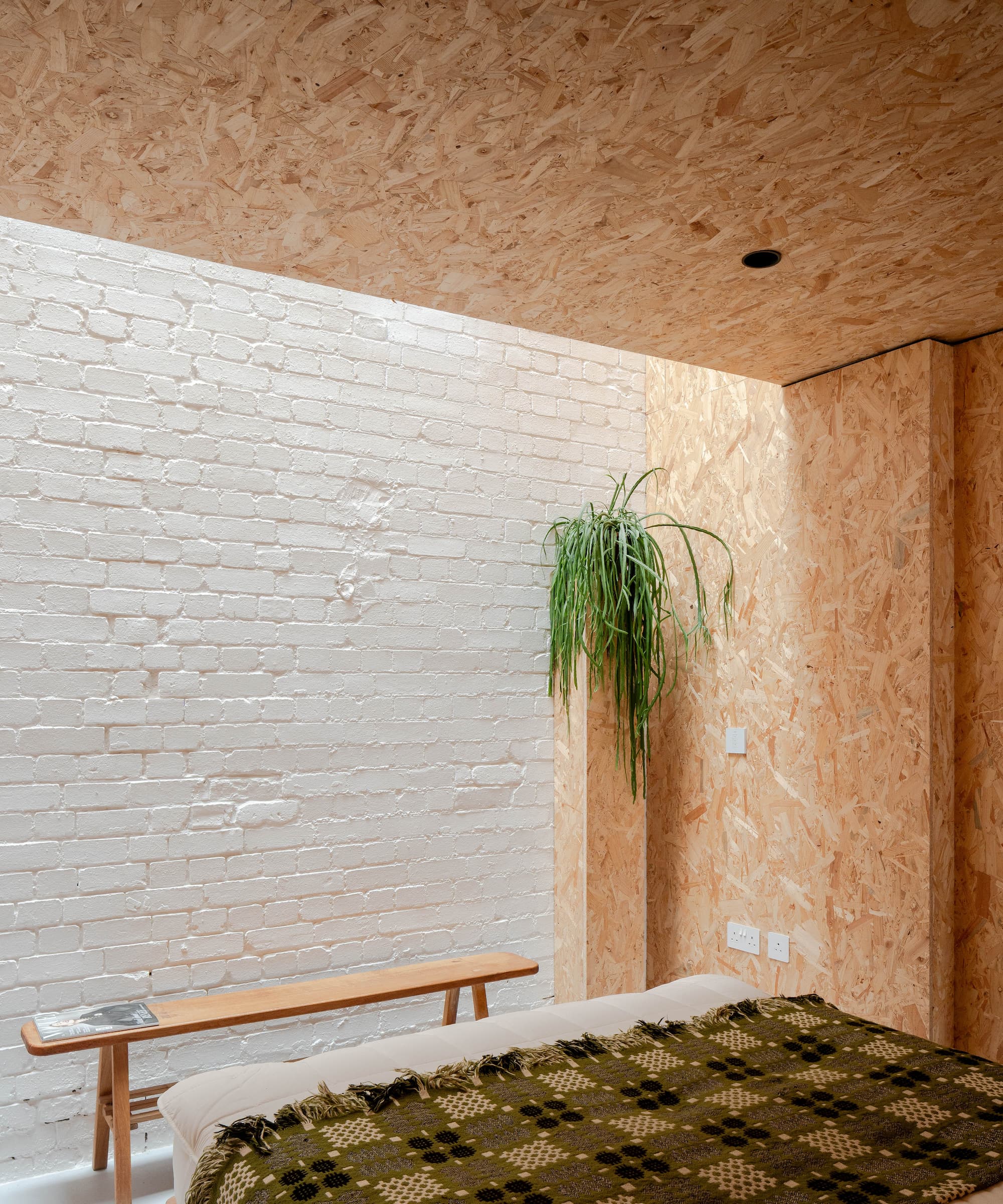 A bedroom with a white brick wall and a plasterboard wall with a plant stand next to the wall