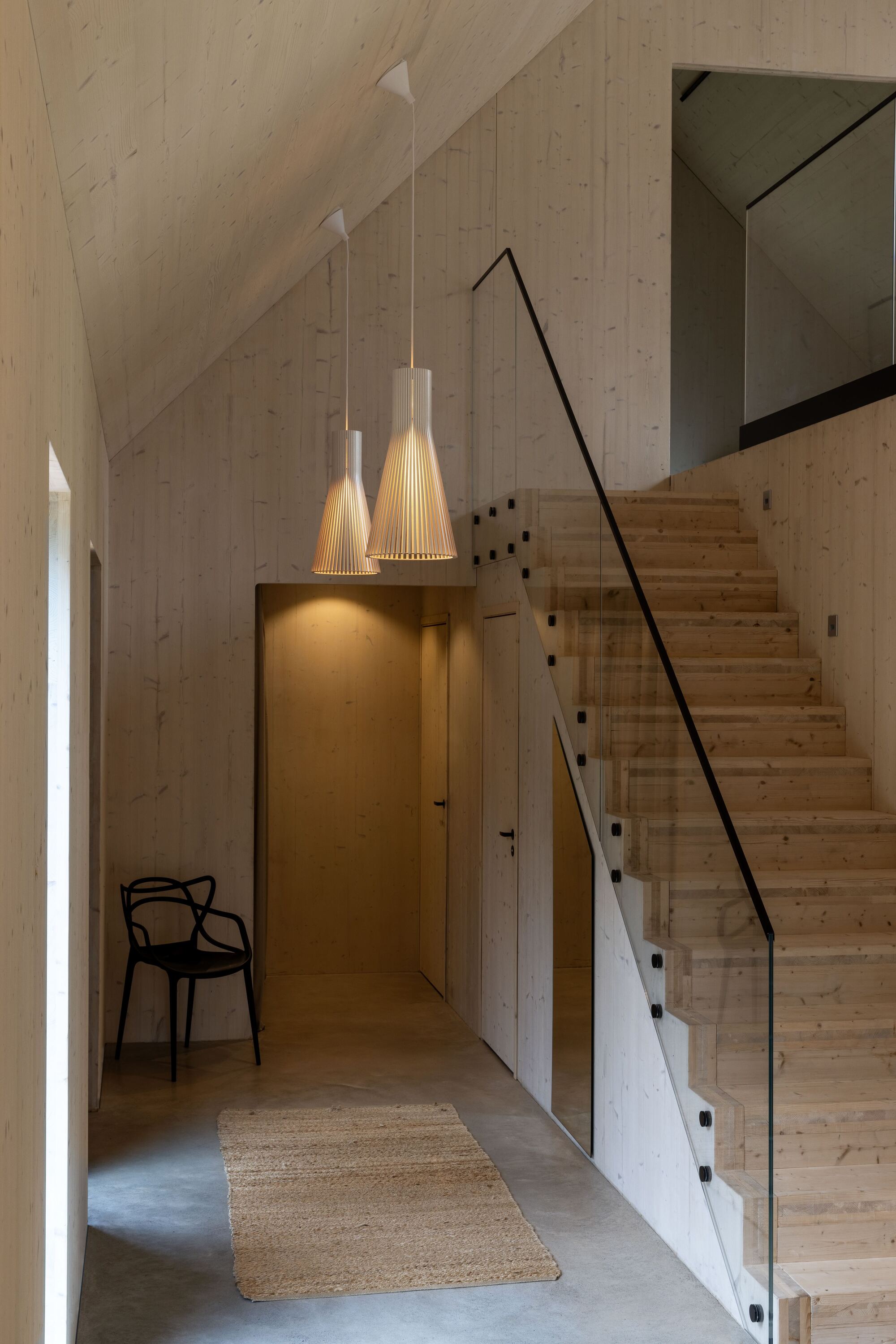 scandi interior with pine stairs, glass balustrade, polished concrete floors, jute rug, pine-clad walls and birch pendant lights