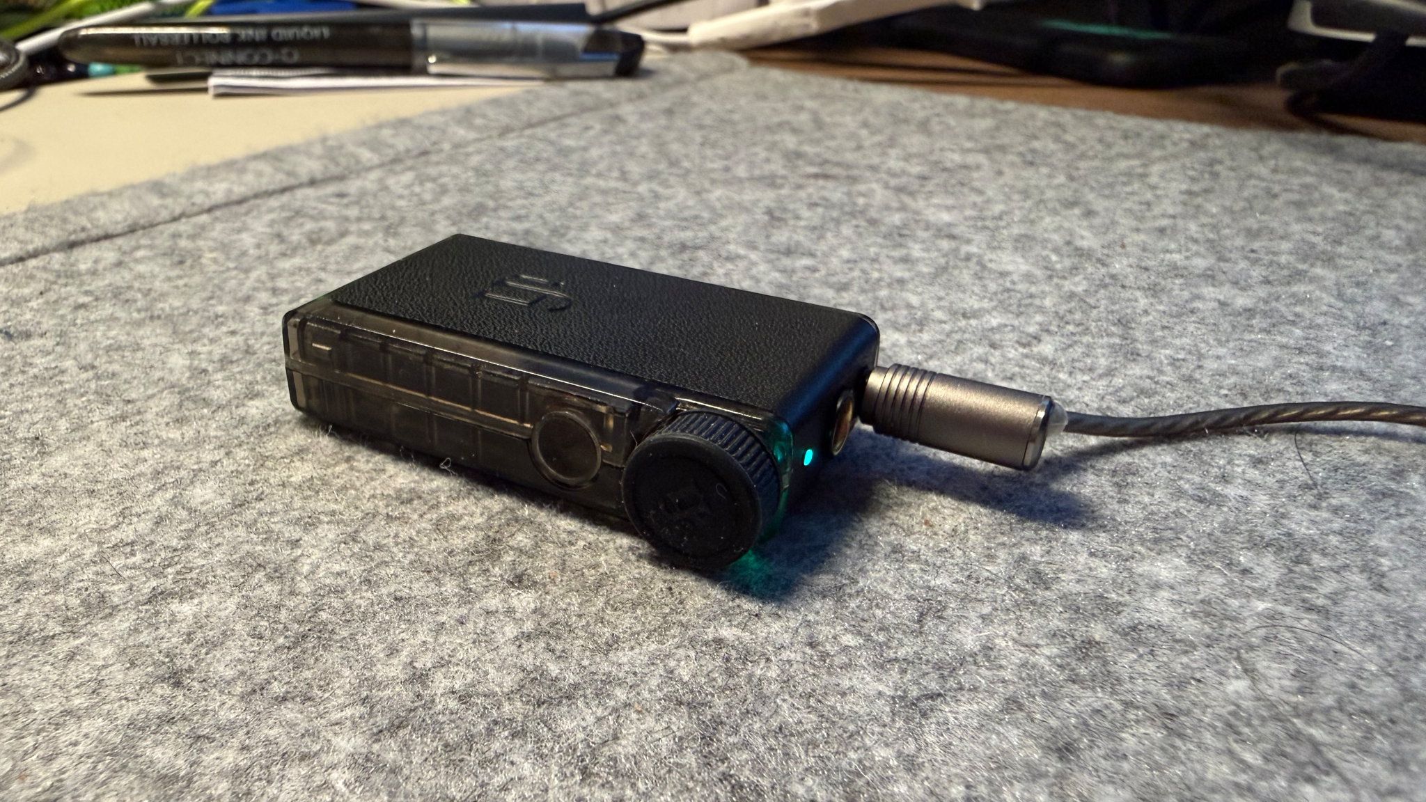 The iFi GO Blu Air laid on a grey desk mat with headphones/IEMs connected to its 3.5mm output