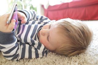 A young boy lying on the floor while looking at a phone screen