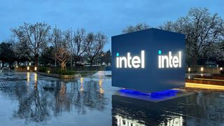 A large cube-shaped sign with the words Intel displayed in neon letters, sits outside of a building in a rainy day