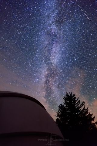 A Perseid meteor crosses the Milky Way in the night sky above an observation dome at Cherry Spring State Park.