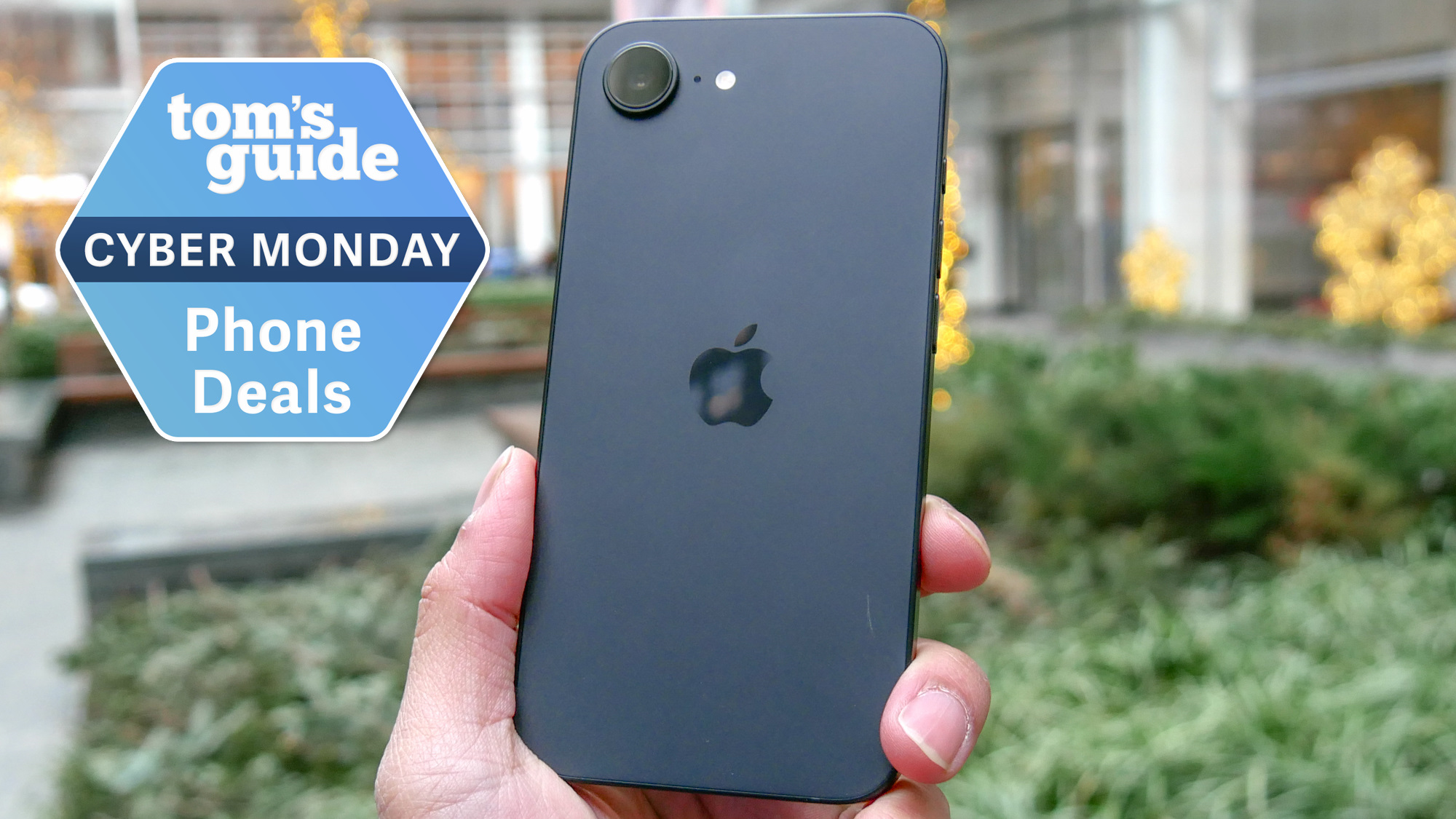 iPhone 16e held in the hand with Cyber Monday badge nearby.
