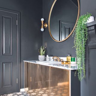 Black bathroom with gold storage unit and matching gold mirror.
