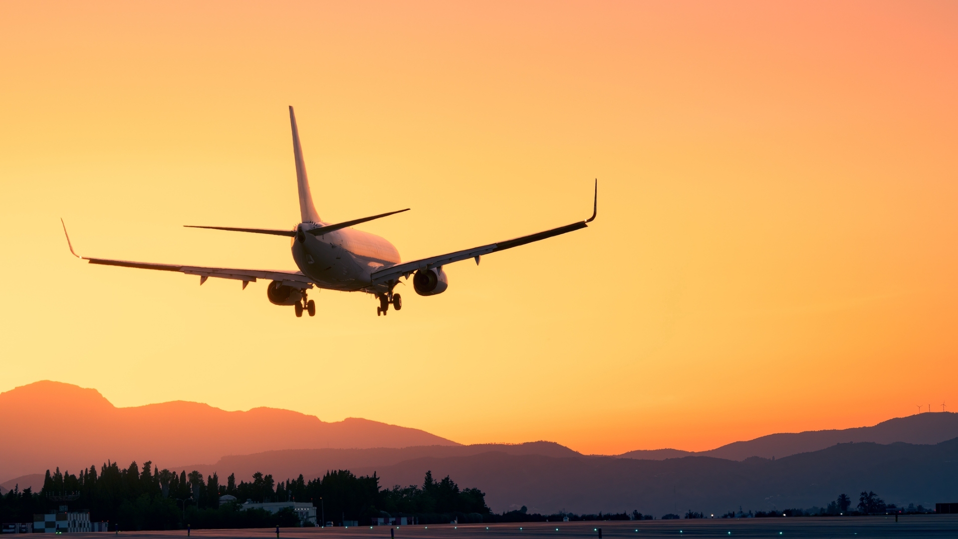 Amidst a breathtaking sunset, an airplane lands gracefully, with majestic mountains as a backdrop.