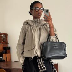 Woman in beige anorak holding a phone and black bag