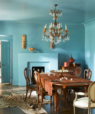 Turquoise painted dining room with dark wooden furniture, chandelier, animal print rug, wooden flooring