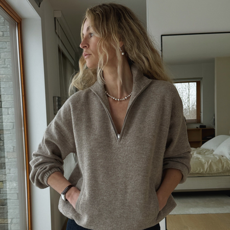 Woman wearing brown quarter-zip sweater outfit with jeans, sweater, and pearl necklace.