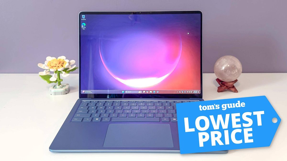 Microsoft Surface Laptop 7 open on table with flower and and orb next to it with Tom&#039;s Guide Lowest Price badge