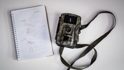 Trail camera on a table next to a notebook with drawings of birds in