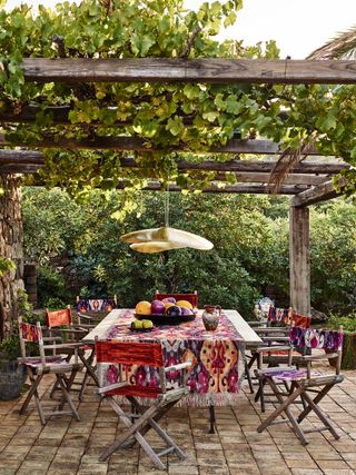 Boho-syle patio table and chairs underneath a rustic pergola draped in vines.