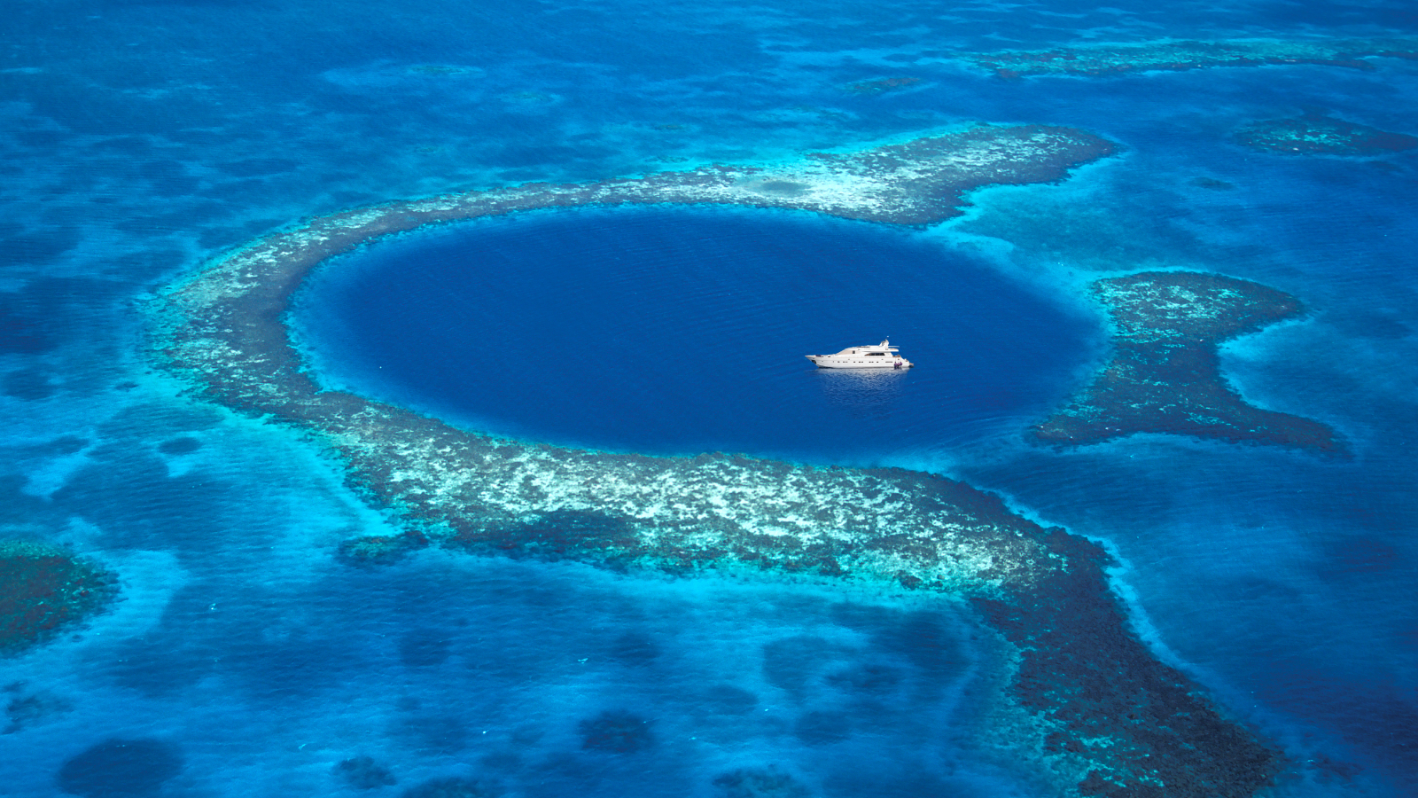 An aerial photo of the Great Blue Hole with a boat in its center